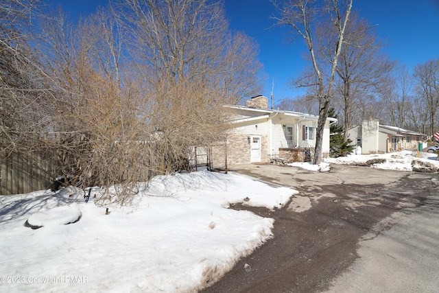 view of snowy exterior with driveway and a chimney