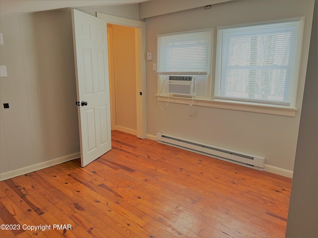 empty room with baseboards, light wood-style flooring, a baseboard heating unit, and cooling unit