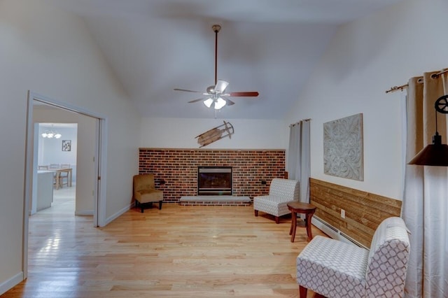 living area with high vaulted ceiling, ceiling fan, a baseboard radiator, a brick fireplace, and wood finished floors