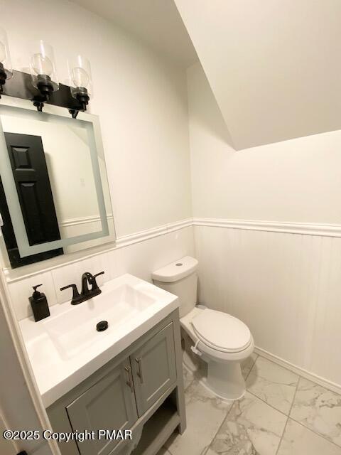 half bathroom featuring toilet, marble finish floor, wainscoting, and vanity