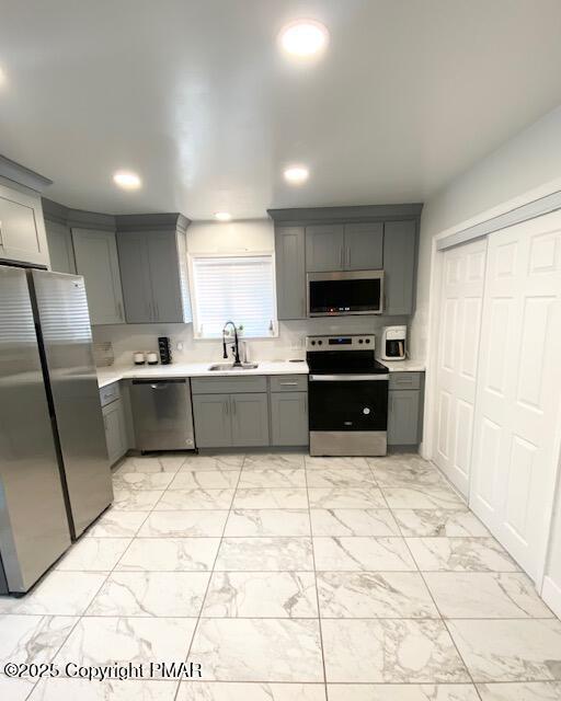 kitchen featuring gray cabinets, stainless steel appliances, a sink, and light countertops