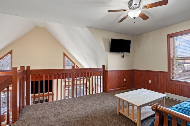 living area with wooden walls, carpet, lofted ceiling, wainscoting, and a ceiling fan