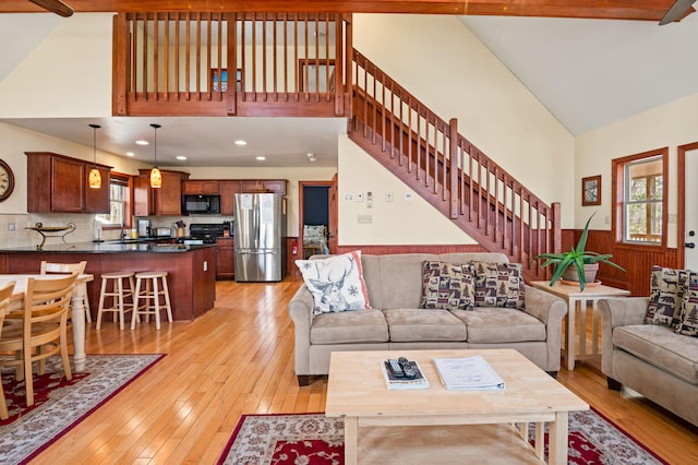 living area featuring a wainscoted wall, high vaulted ceiling, recessed lighting, stairs, and light wood-style floors