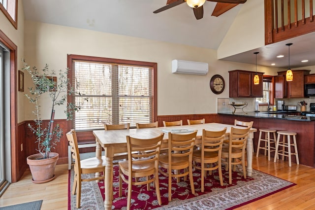 dining space with light wood-style floors, a ceiling fan, an AC wall unit, and wainscoting