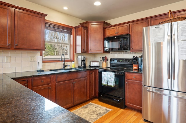 kitchen featuring dark stone counters, light wood-style flooring, a sink, black appliances, and backsplash