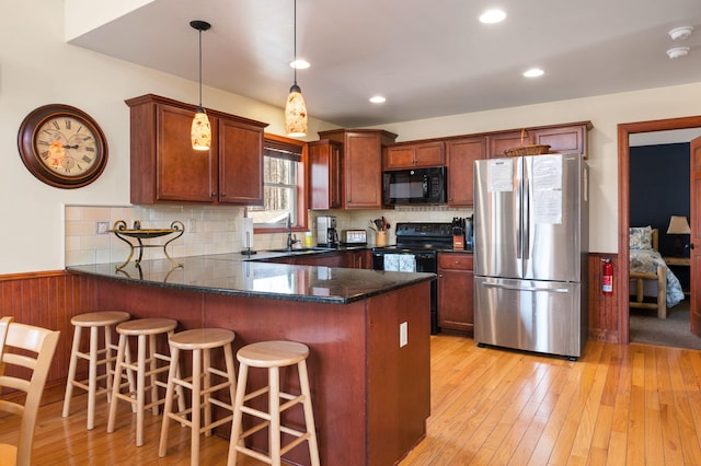 kitchen featuring backsplash, light wood-style flooring, a peninsula, and black appliances