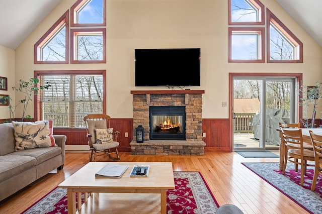 living area featuring a stone fireplace, a wainscoted wall, wood-type flooring, and high vaulted ceiling