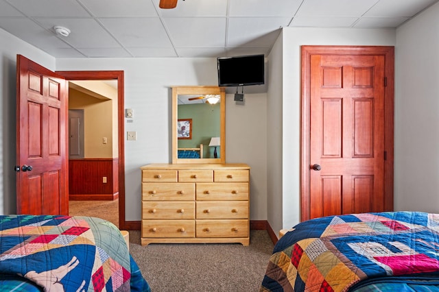 carpeted bedroom with electric panel, a drop ceiling, wooden walls, and a wainscoted wall