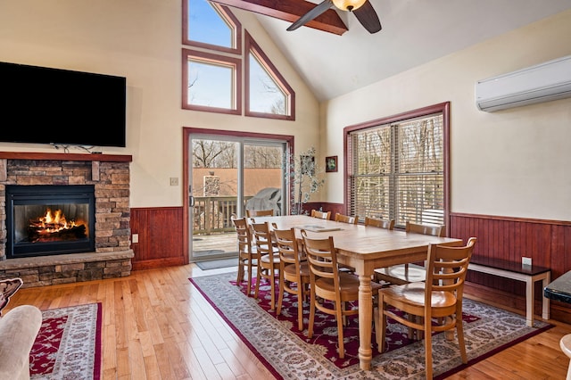 dining room with a ceiling fan, hardwood / wood-style flooring, a wall mounted AC, a stone fireplace, and wainscoting