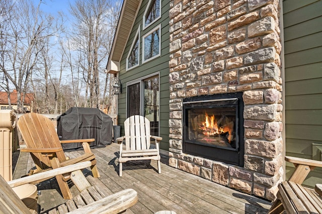 wooden deck featuring a glass covered fireplace and area for grilling