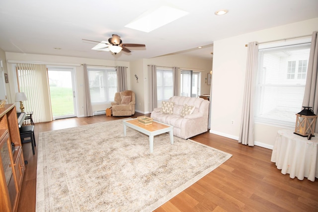 living room featuring a ceiling fan, wood finished floors, recessed lighting, a skylight, and baseboards