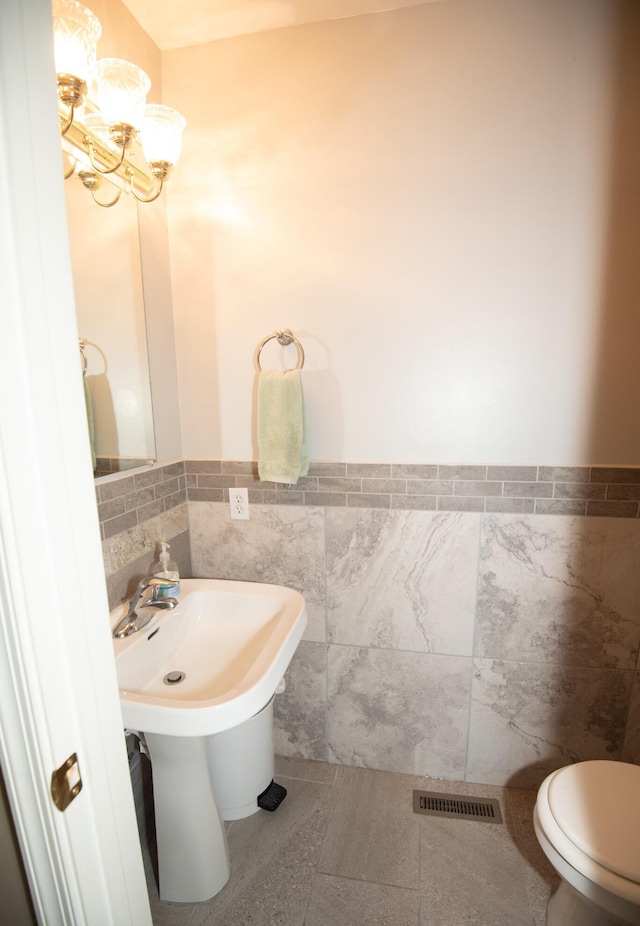 bathroom with visible vents, a wainscoted wall, toilet, a notable chandelier, and tile walls