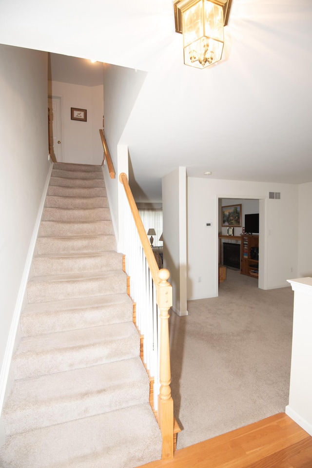 stairway with visible vents, carpet flooring, and an inviting chandelier