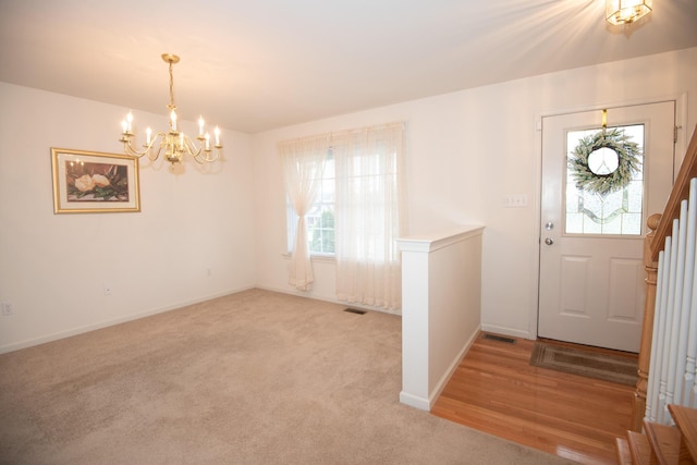 foyer entrance with visible vents, light carpet, a notable chandelier, and baseboards