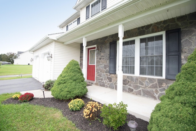 view of exterior entry with covered porch, stone siding, and driveway