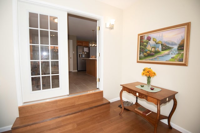 hallway featuring a chandelier, baseboards, and wood finished floors