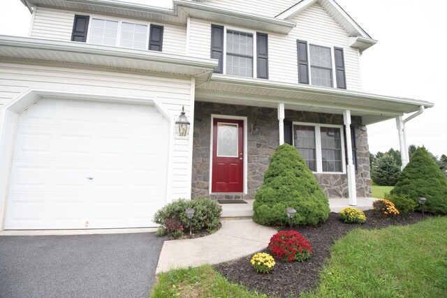 view of front facade featuring aphalt driveway, stone siding, a porch, and an attached garage