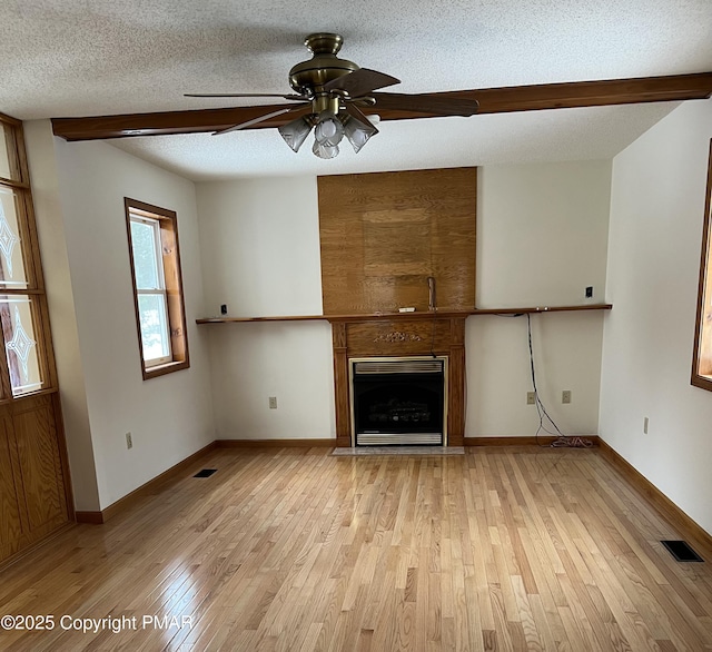 unfurnished living room with beamed ceiling, a fireplace, a textured ceiling, and light wood-type flooring