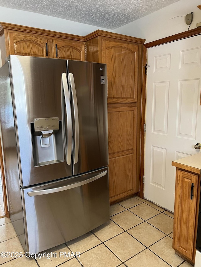 kitchen featuring stainless steel refrigerator with ice dispenser, light tile patterned floors, light countertops, brown cabinetry, and a textured ceiling