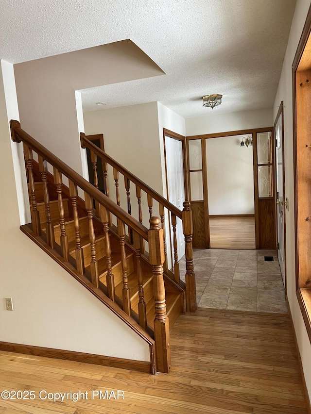 stairs with a textured ceiling and wood finished floors