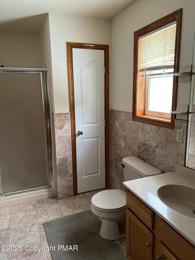 bathroom featuring tile walls, vanity, a shower with door, and toilet