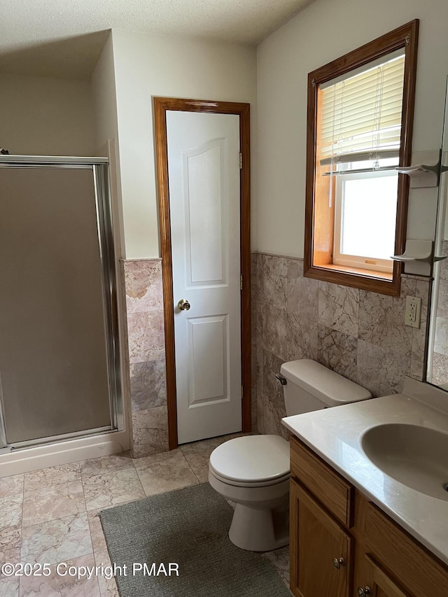 bathroom with a stall shower, wainscoting, tile walls, and vanity