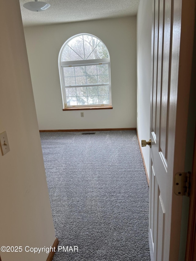 carpeted empty room with a textured ceiling, visible vents, and baseboards