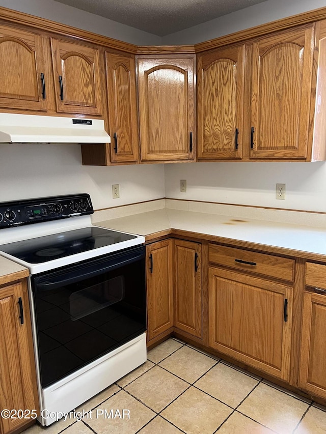 kitchen featuring light tile patterned flooring, under cabinet range hood, electric range, light countertops, and brown cabinets