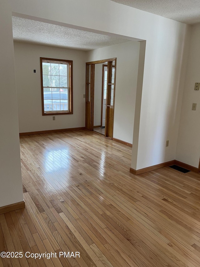 unfurnished room with baseboards, light wood-style flooring, and a textured ceiling