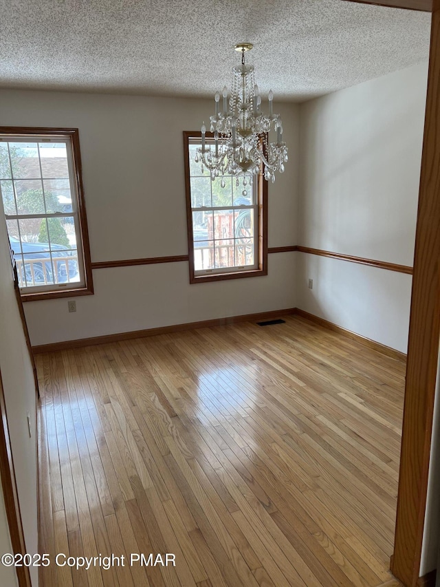 spare room with an inviting chandelier, a textured ceiling, and light hardwood / wood-style floors