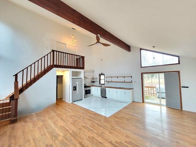 unfurnished living room featuring ceiling fan, high vaulted ceiling, stairway, light wood-type flooring, and beamed ceiling