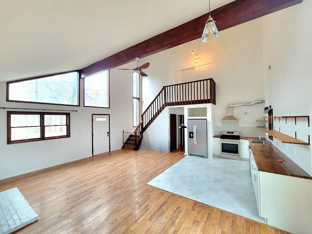 kitchen featuring light wood-style flooring, stainless steel appliances, a sink, tasteful backsplash, and beamed ceiling