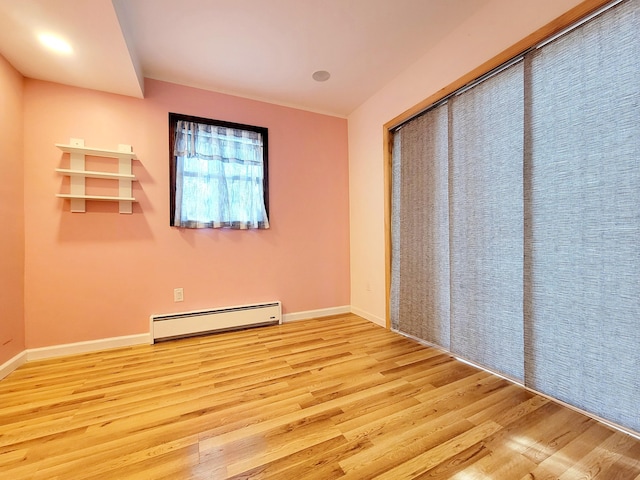 spare room featuring a baseboard radiator, baseboards, and wood finished floors