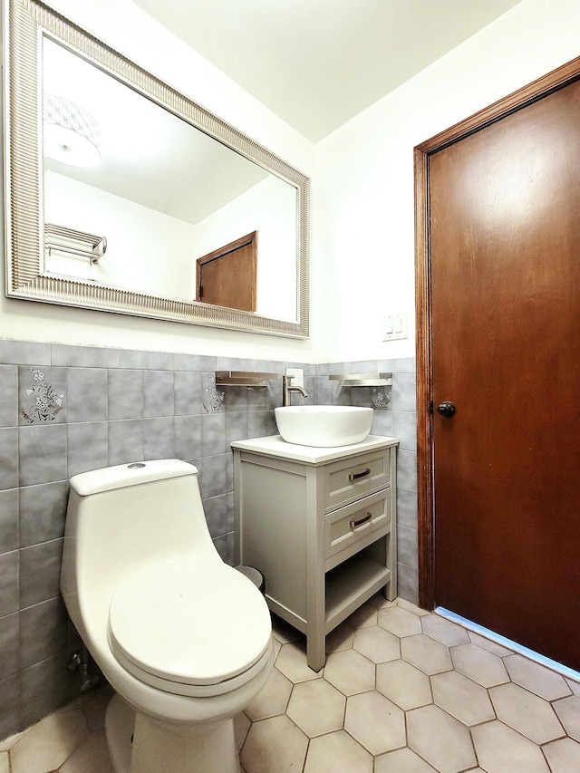 half bathroom with tile walls, toilet, wainscoting, vanity, and tile patterned floors