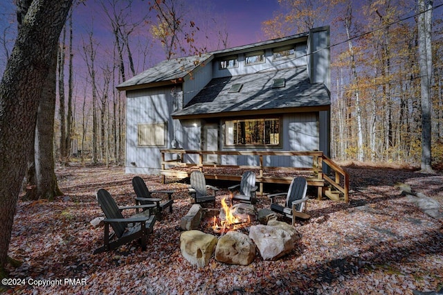 rear view of house with an outdoor fire pit, a deck, and roof with shingles