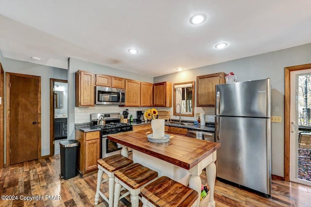 kitchen with decorative backsplash, appliances with stainless steel finishes, a sink, wood finished floors, and butcher block countertops