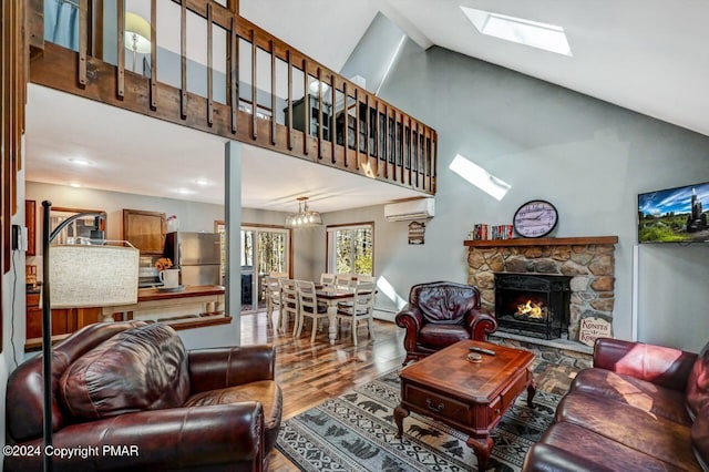 living area featuring a skylight, a fireplace, wood finished floors, high vaulted ceiling, and a wall mounted air conditioner