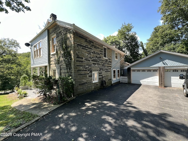 view of property exterior featuring a garage, an outbuilding, stone siding, and a chimney