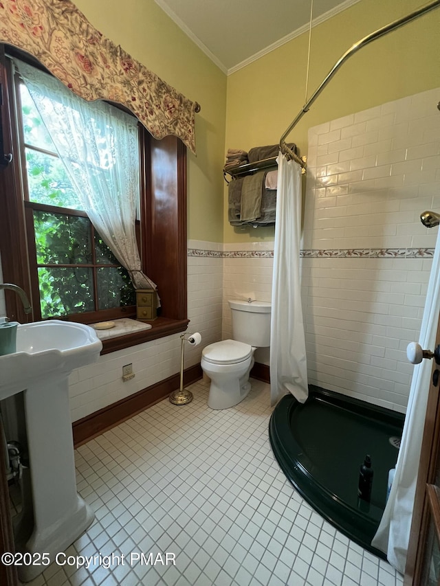 bathroom with ornamental molding, a wainscoted wall, toilet, and tiled shower