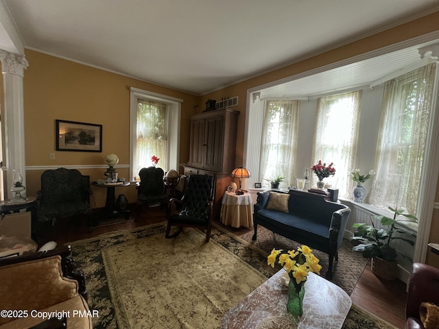 living area with ornate columns, ornamental molding, and wood finished floors