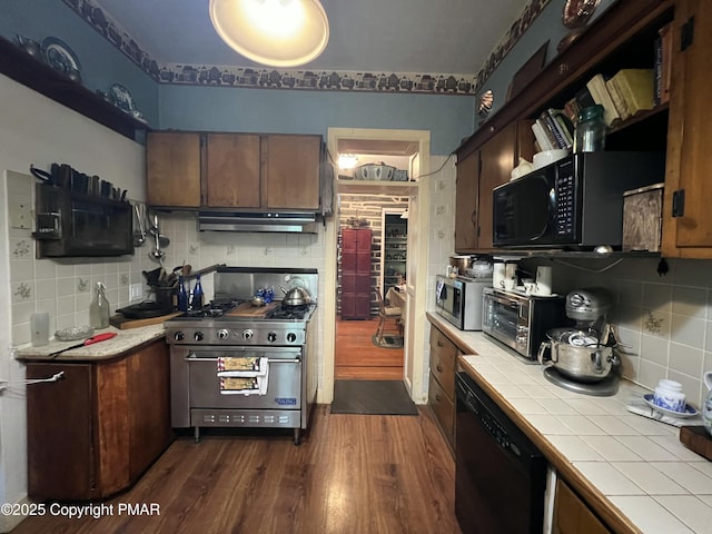 kitchen featuring dark wood finished floors, decorative backsplash, tile countertops, under cabinet range hood, and black appliances