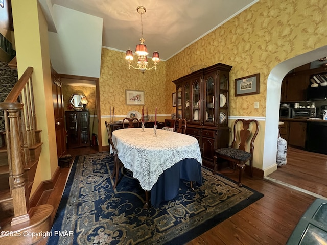 dining area with arched walkways, stairway, dark wood-style floors, and wallpapered walls