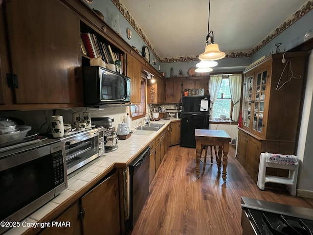 kitchen with decorative light fixtures, light wood finished floors, tile counters, a sink, and black appliances