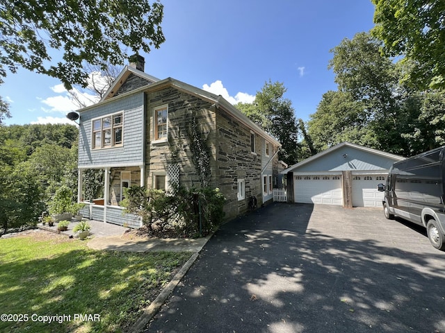 view of side of property featuring a garage, stone siding, a chimney, an outbuilding, and a porch