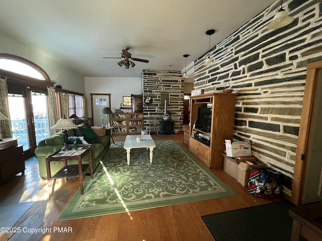 living room with wood finished floors, a wood stove, and a ceiling fan