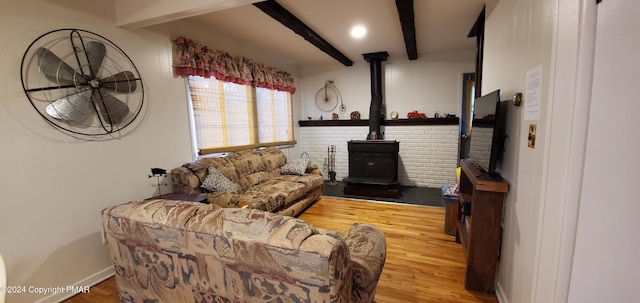 living area featuring a wood stove, baseboards, beam ceiling, and wood finished floors