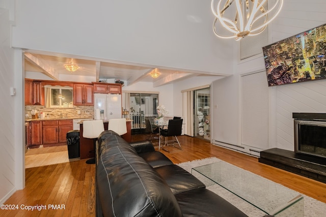 living area with a fireplace with raised hearth, light wood-style flooring, a notable chandelier, baseboard heating, and beam ceiling