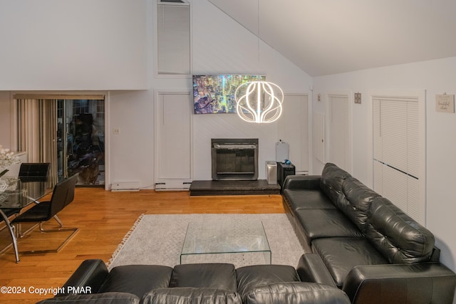 living room with high vaulted ceiling, wood finished floors, a glass covered fireplace, and an inviting chandelier