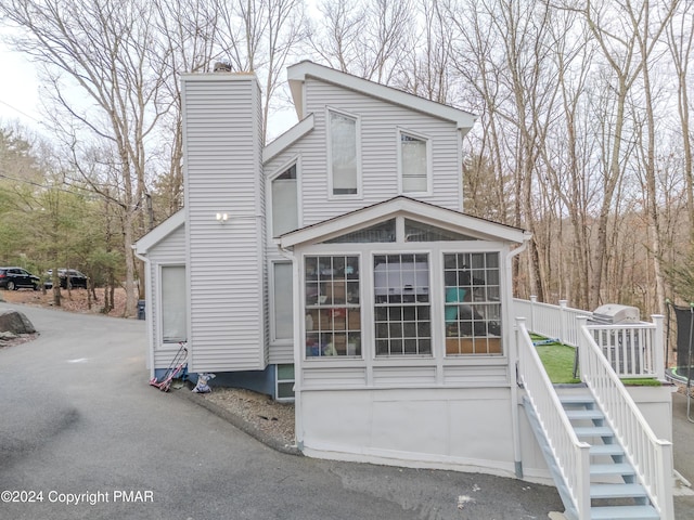 view of front of house with stairs, a chimney, and a sunroom