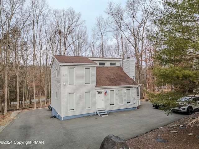 view of front of house with entry steps, driveway, and roof with shingles